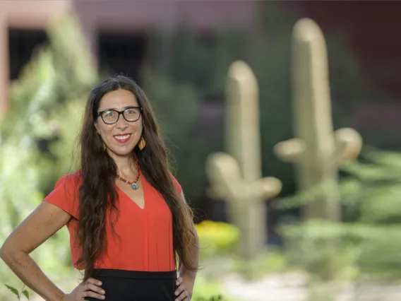 Stephanie Russo Carroll poses in front of saguaro cacti in a red shirt.