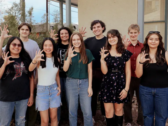 2024 Mo's Policy Scholars pose outside the Udall Center while giving the Wildcats hand signal.