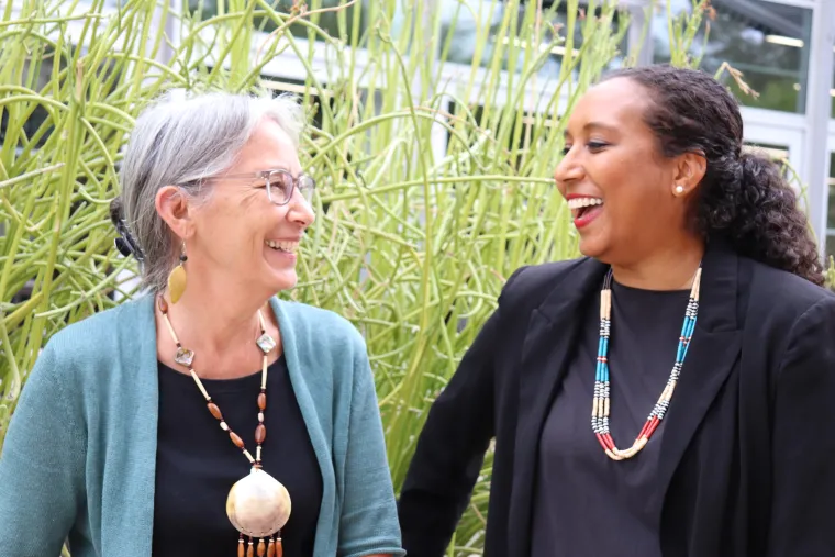 Natsu Tailor Saito and Akilah Kinnison look at each other and laugh in front of a succulent planter at the UArizona law school.