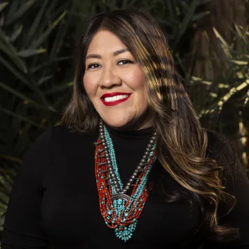 A portrait of Amanda Tachine in a black turtle neck and turquoise and coral beaded necklace.