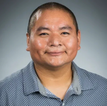 A portrait of Darryl Reano in a blue collared shirt with a white polka dot pattern.